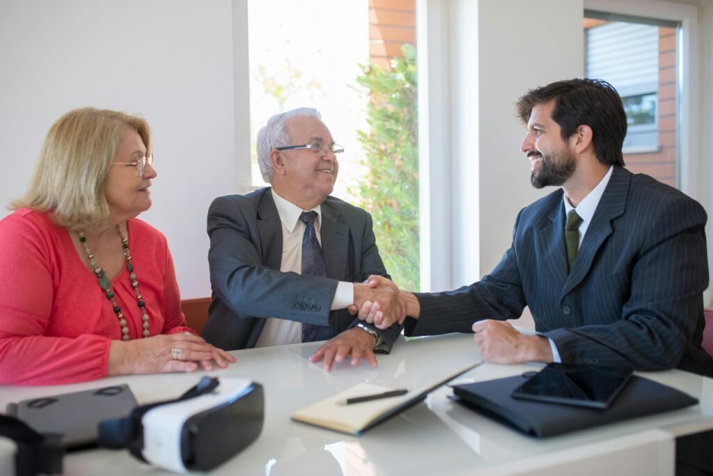 Three business professionals shaking hands during a meeting in an office, symbolizing successful deal-making.