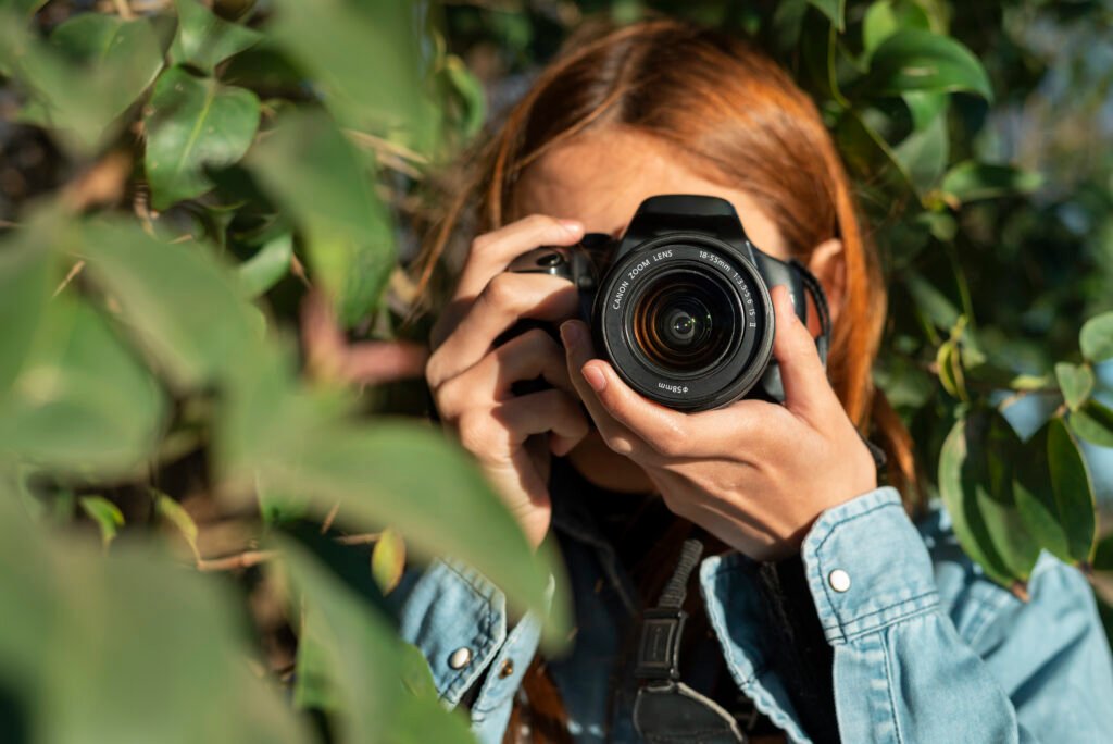 Person holding an camera taking a picture behind a tree.